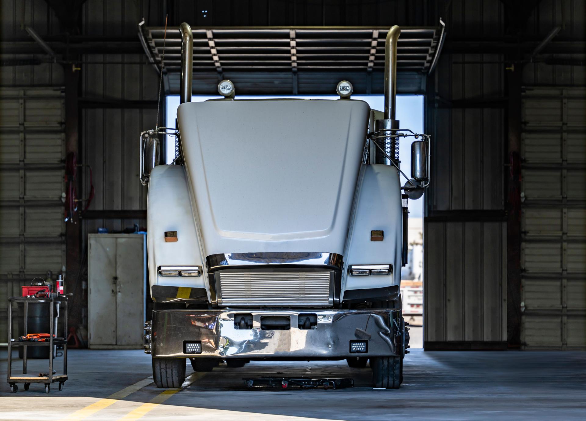 Powerful white big rig semi truck tractor with open hood standing in Mechanical workshop for inspection and maintenance