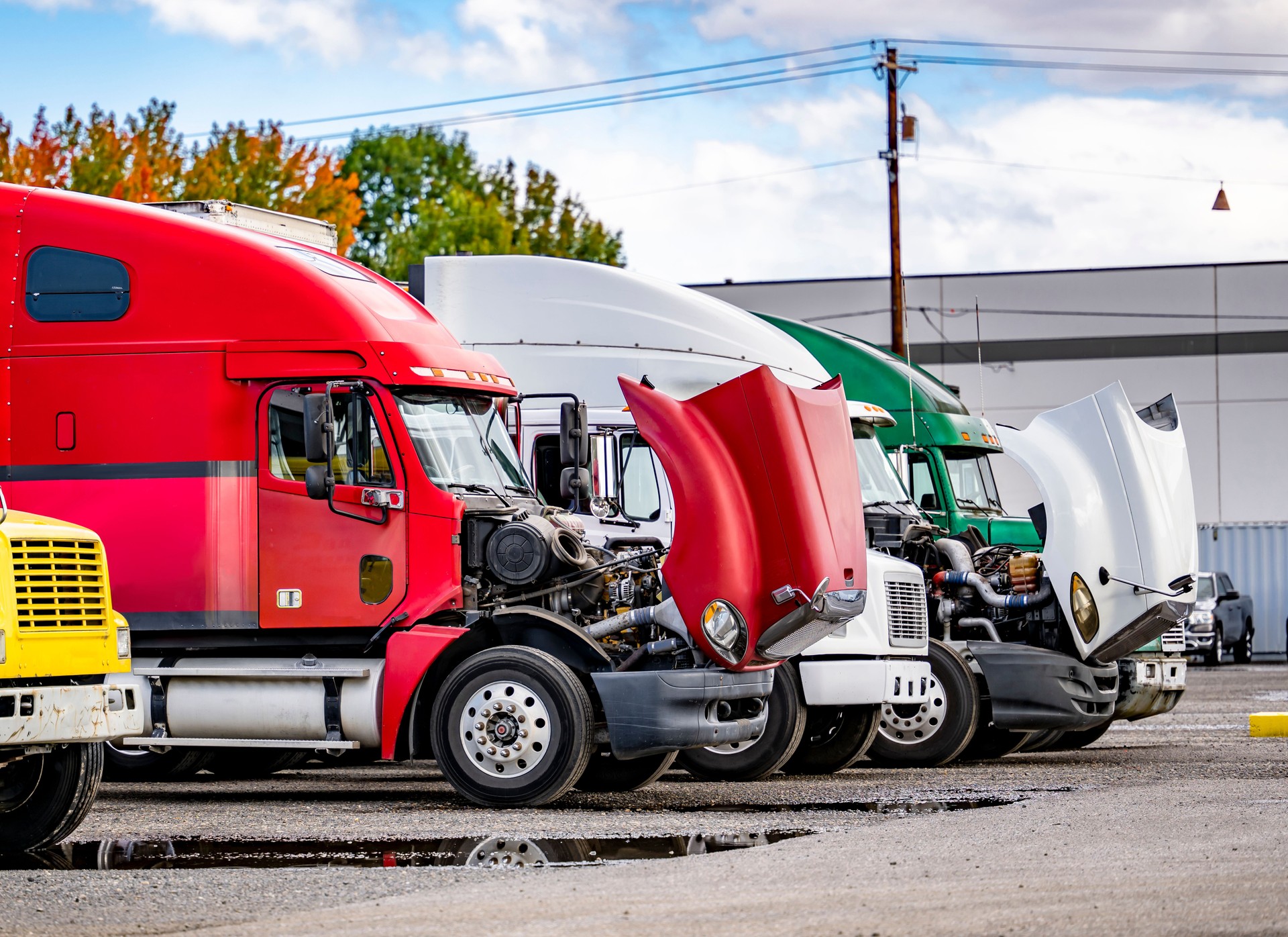 Big rig semi trucks tractors with open hoods standing in row on industrial parking lot waiting for engine repair and transmission maintenance