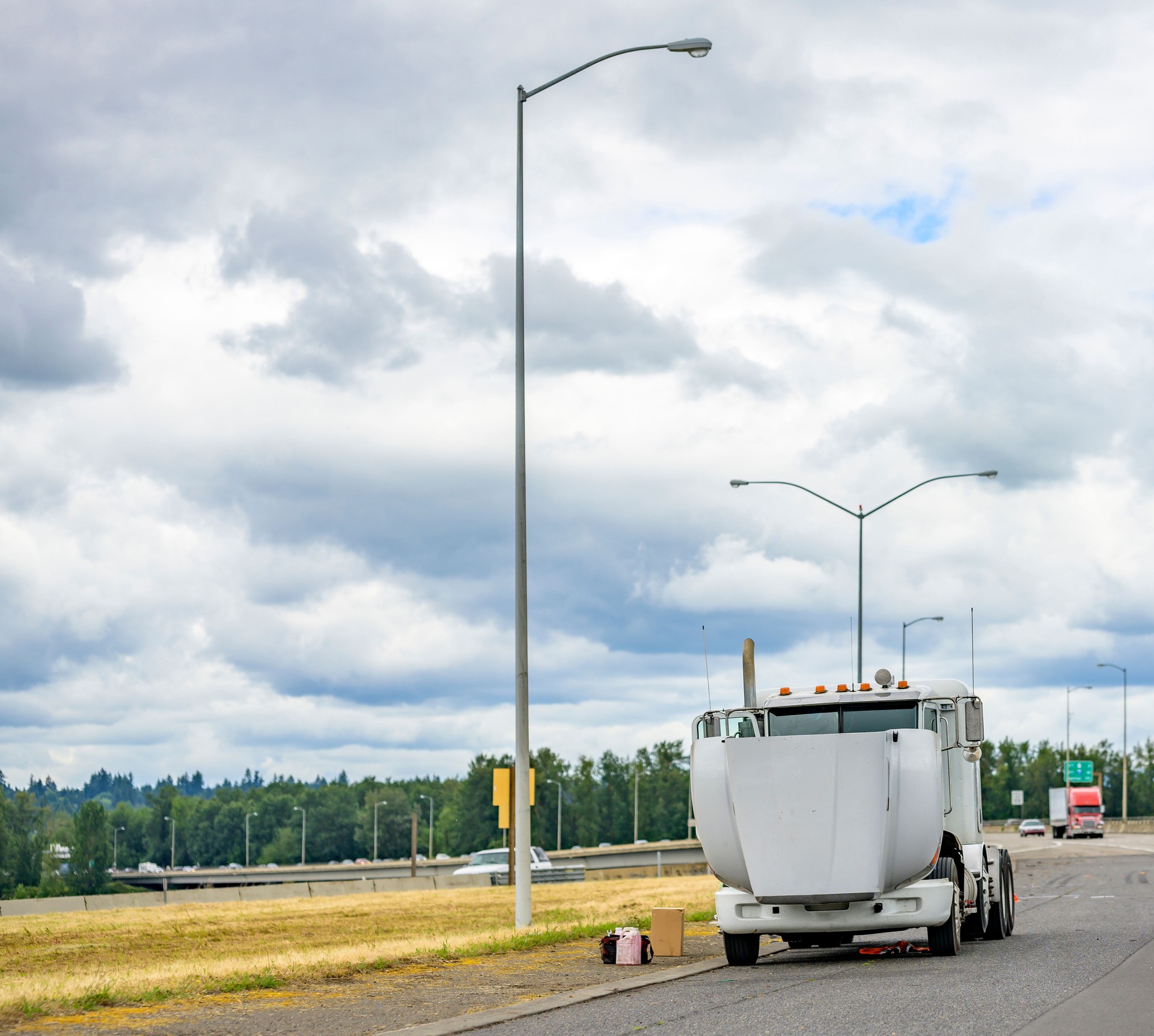 Broken white big rig semi truck tractor with open hood standing on the road shoulder out of service